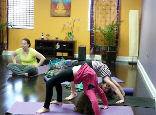 Children and an adult doing yoga poses on mats in a yoga studio