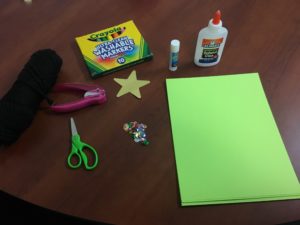 Craft supplies on a table: green construction paper, markers, glue, scissors, a hole punch and a star