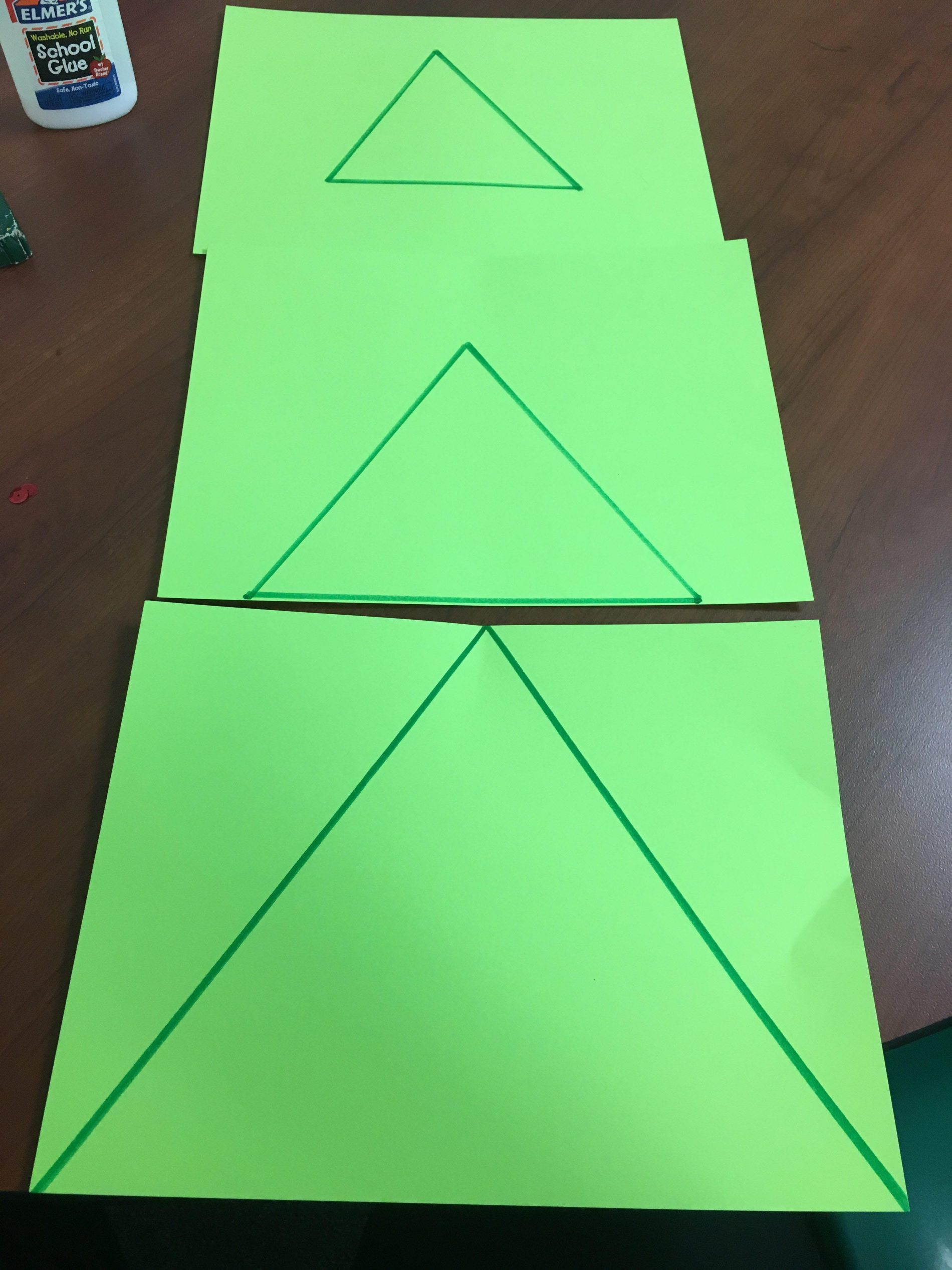Three green paper triangles of different sizes drawn on and stacked to form a tree shape