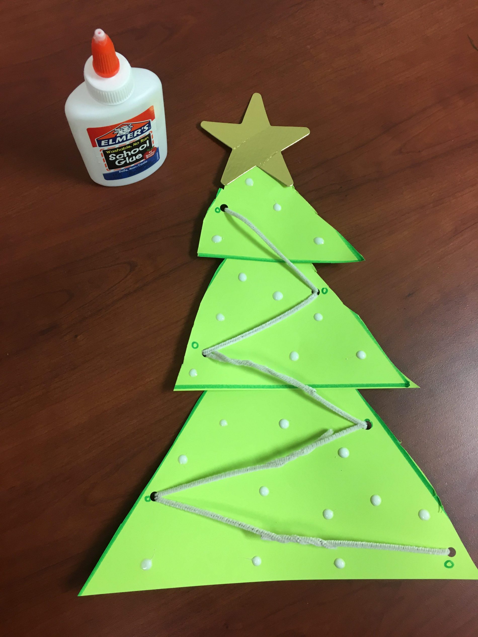 Green paper Christmas tree with white yarn laced through holes and glue dots as ornaments