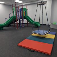 Therapy gym with a platform swing, colorful floor mats and a green slide