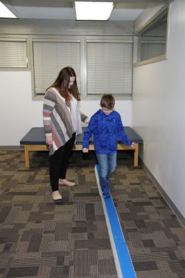 Therapist and a boy walking along a blue tape line on the floor of a therapy room