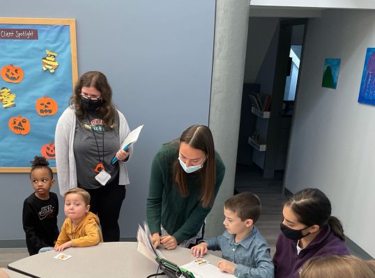 Therapists and young children working together around a table in a classroom decorated with paper pumpkins
