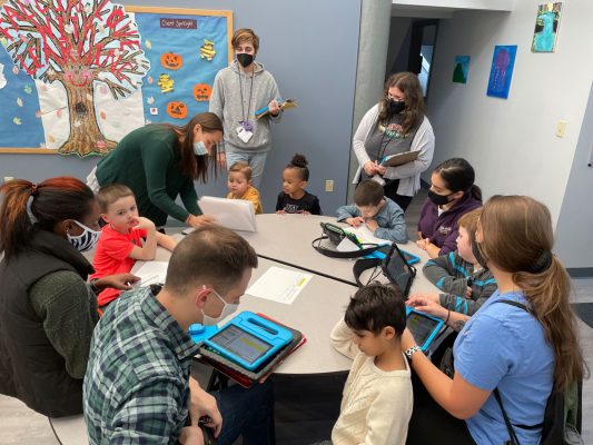 Group of children using tablets with therapists and staff around a round table