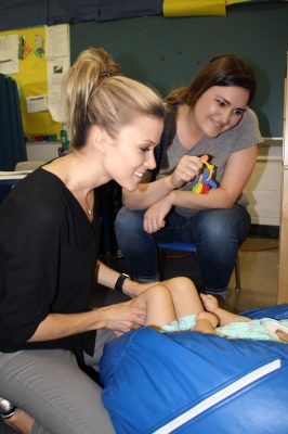 Two therapists smiling as they work with a child lying on a blue bean bag