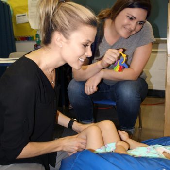 Two therapists smiling as they work with a child lying on a blue bean bag