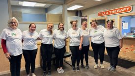 Eight LLA Therapy staff members in white shirts posing in front of the LLA Therapy front desk