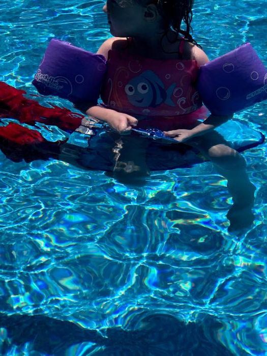 Child in arm floaties sitting in a swimming pool