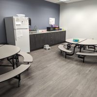 Break room with round tables with attached benches and a counter along the back wall