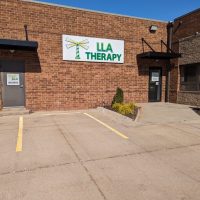 Brick office building exterior with a green LLA Therapy sign above a parking area