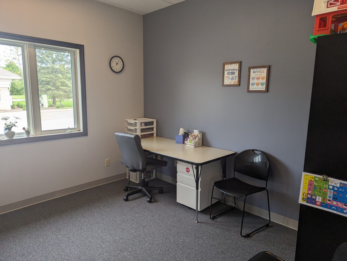 Therapy room with a desk, rolling chair, black chair and framed art on gray walls
