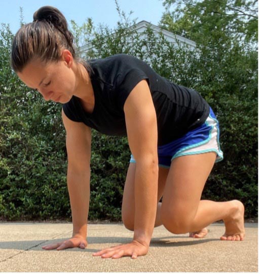 Woman on her hands and feet in a bear crawl position outdoors on pavement