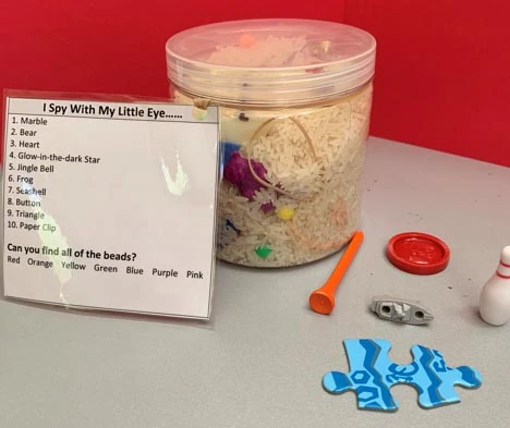 Plastic jar of rice with hidden small objects beside an I Spy checklist card