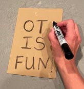 Hand writing OT is fun! on a piece of cardboard with a marker
