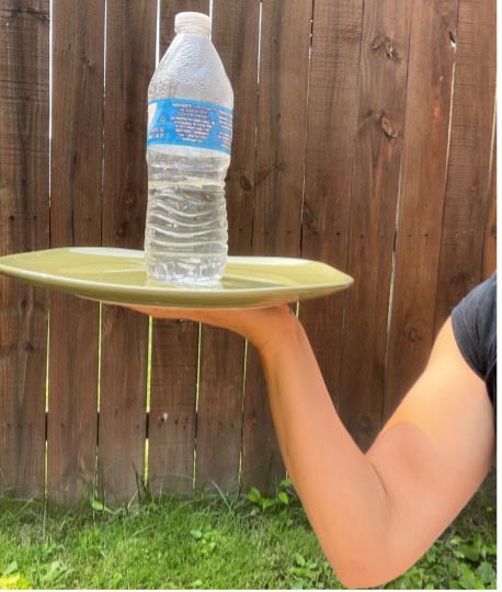 Arm holding a plate with a water bottle balanced on it outdoors