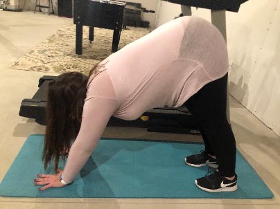 Woman on a teal mat with hands and feet on the floor and hips raised, demonstrating a bear crawl