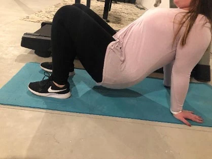 Woman on a teal mat with hands and feet on the floor and belly facing up, demonstrating a crab walk