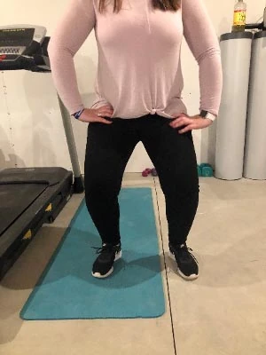 Person standing with feet apart and hands on hips on a teal mat