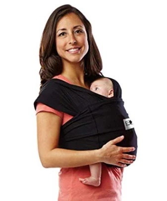 Smiling woman carrying an infant in a black wrap-style baby carrier