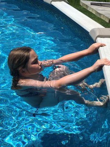 Girl in a swimming pool holding the edge with her arms while kicking