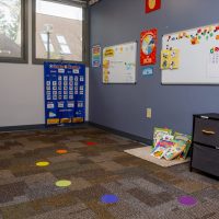Classroom-style therapy room with a calendar wall and colored dots on the carpet