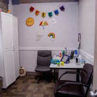 Small office with a desk, chairs and a cabinet and children's art on the wall