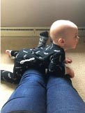 Baby lying on his tummy beside an adult's legs
