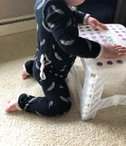 Baby kneeling and reaching up toward a white step stool