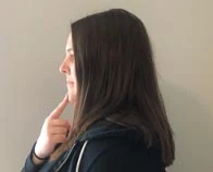 Woman in side view with a finger on her chin to demonstrate a chin tuck