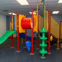 Indoor play structure with slides and a climbing pole in a therapy gym