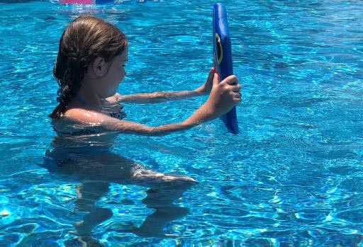 Girl standing in a pool holding a blue kickboard upright