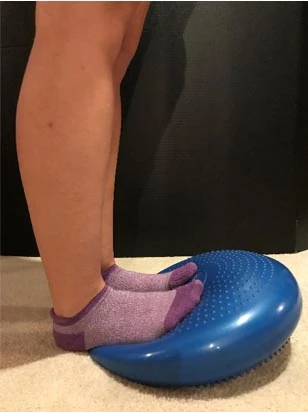Child's feet in purple socks standing on a blue inflatable balance disc