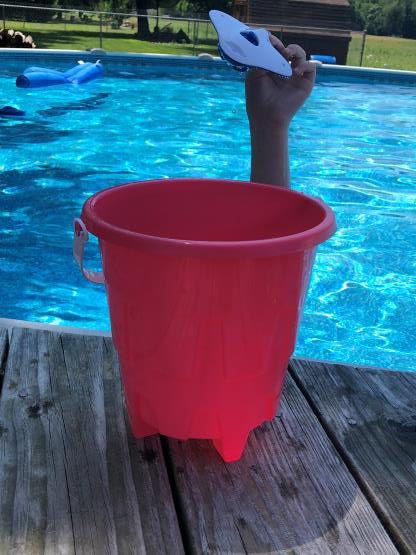 Arm reaching out of a swimming pool holding a blue kickboard above a red bucket on the dock