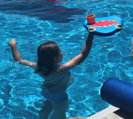 Girl in a pool holding a kickboard with a cup on it above her head